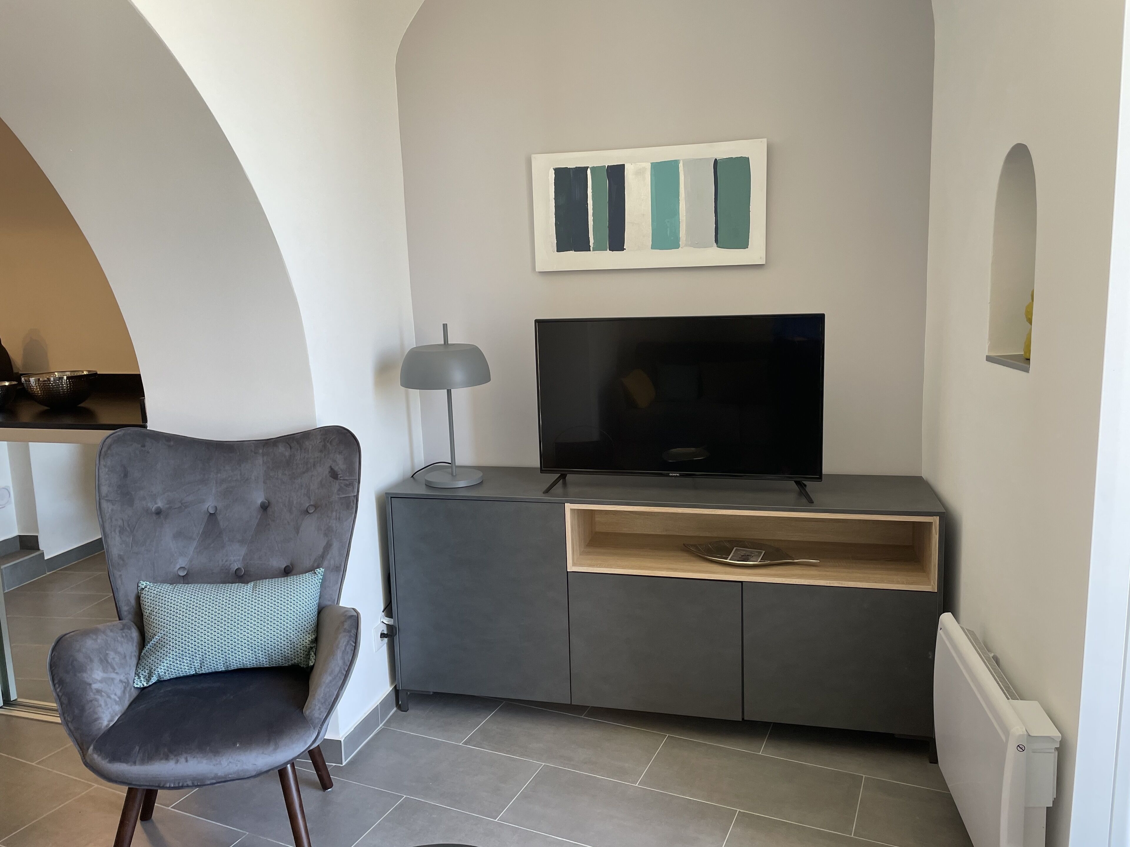 A modern living room with a grey sofa, a flat-screen TV, and a minimalist artwork on the wall.