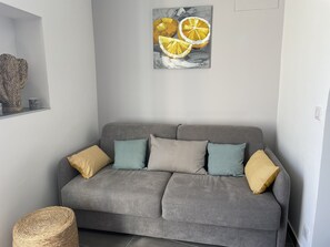 A grey sofa with patterned cushions, a woven basket, and a painting of lemons on the wall.