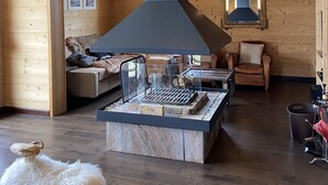 A cozy living room with a fireplace, wooden walls, a sofa, a chair, and a fluffy white stool. - Contemporary chalet, panoramic view (ORMONT DESSOUS)