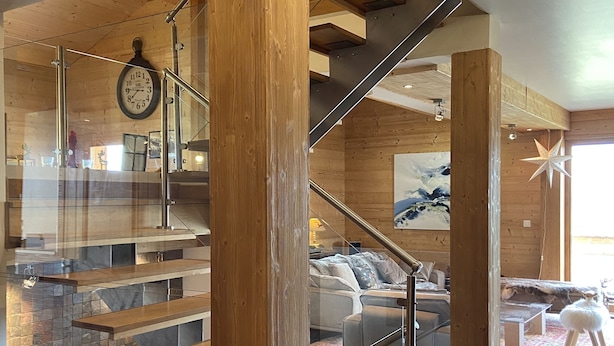 A modern interior with a wooden staircase, a living area with a sofa and a rug, and a clock on the wall. - Contemporary chalet, panoramic view (ORMONT DESSOUS)