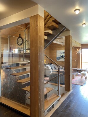 A modern interior with a wooden staircase, a living area with a sofa and a rug, and a clock on the wall. - Contemporary chalet, panoramic view (ORMONT DESSOUS)