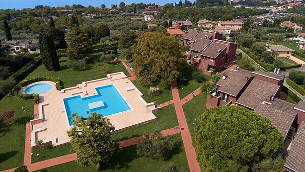 An aerial view of a residential area with a large swimming pool surrounded by well-maintained lawns and trees. - Regarda - Blue View 2 with lake view, 2 bedrooms, pool (Bardolino)
