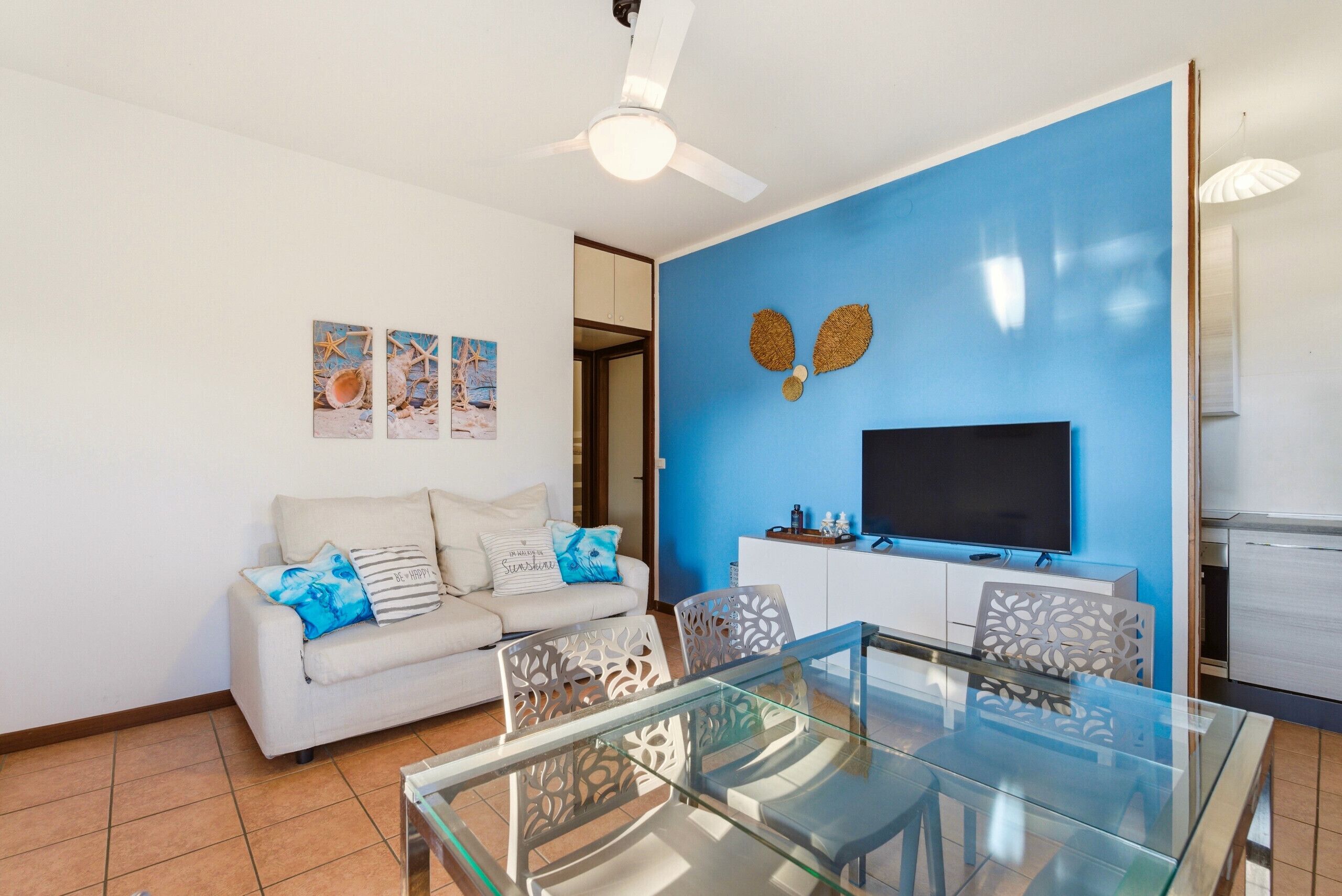 A living room with a glass dining table, white sofa, and a flat-screen TV.