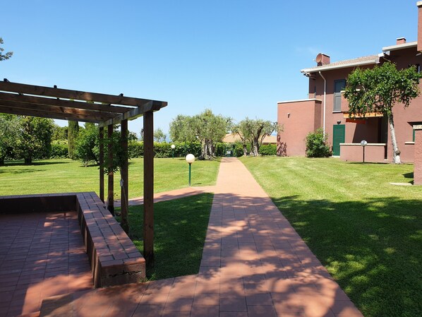 A pathway leading to a building with a brick facade and a covered area with a pergola.