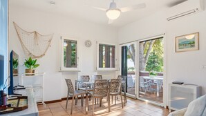 A bright room with a ceiling fan, a dining table with chairs, a TV, and a sliding glass door leading to an outdoor area. - Regarda - Blue View 2 with lake view, 2 bedrooms, pool (Bardolino)