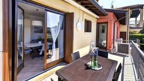 Un espace repas comprenant une table et des chaises, une porte-fenêtre coulissante donnant sur un espace intérieur, et un balcon doté d’une balustrade.