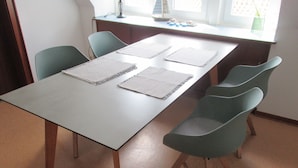 A conference table with four chairs, a window with blinds, and a desk with a lamp and decorative items. - Modern apartment on the 1st floor, 3 rooms + dining area, kitchen w. Dishwasher, bathroom (Cuxhaven)