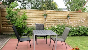 A patio with a table and two chairs, surrounded by a wooden fence and greenery. - Modern apartment on the 1st floor, 3 rooms + dining area, kitchen w. Dishwasher, bathroom (Cuxhaven)