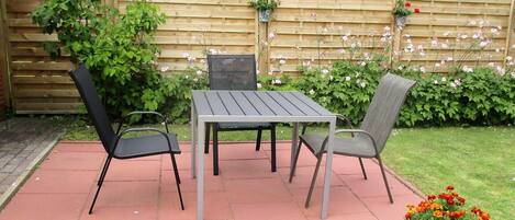 Eine Terrasse mit Tisch und zwei Stühlen, umgeben von einem Holzzaun und Grünpflanzen.