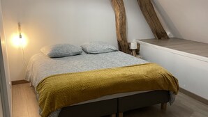 Une chambre à coucher avec un lit, un plafond avec des poutres en bois et un luminaire suspendu.