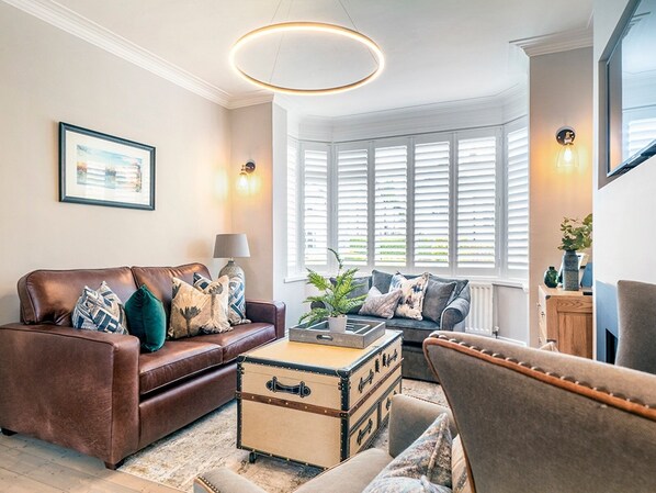 Un salón acogedor con un sofá de cuero marrón, un baúl antiguo y un sillón gris.