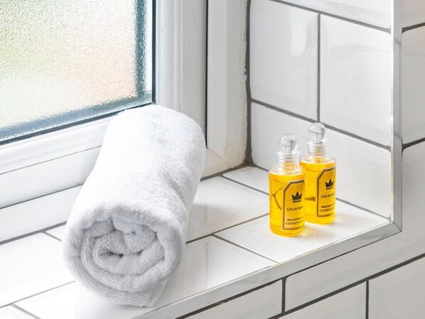 A white towel rolled up on a white tiled ledge next to two bottles of Goldcrest shampoo and conditioner. - Exceptional Villa on Charming Tree-Lined Avenue - Pass the Keys (Belfast)