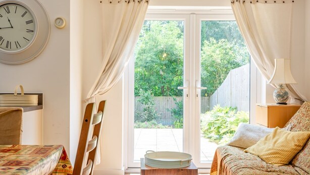 Una habitación con cama, una mesa, una silla, un reloj y vista a un jardín por una puerta corredera.