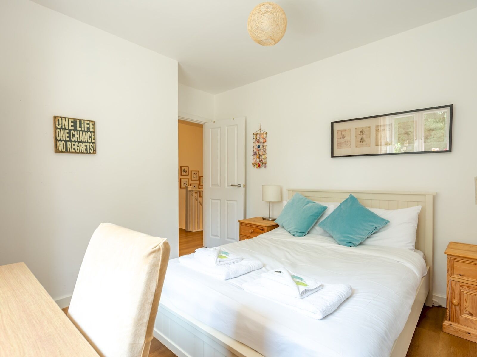 Ein ordentlich eingerichtetes Schlafzimmer mit Bett, Nachttisch, Stuhl und einem an der Wand hängenden Kunstwerk.