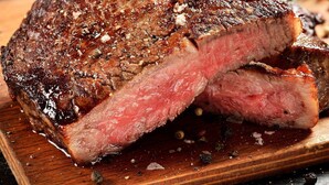 A steak with a crust, cut in half, on a wooden board.
