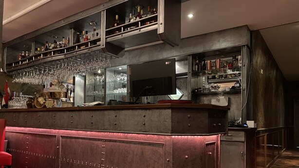 A bar area with a bar counter, shelves with bottles, and a television screen.