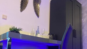 A compact kitchen area with a dark cabinet, a bar counter with blue lighting, a chair, and decorative wall art.