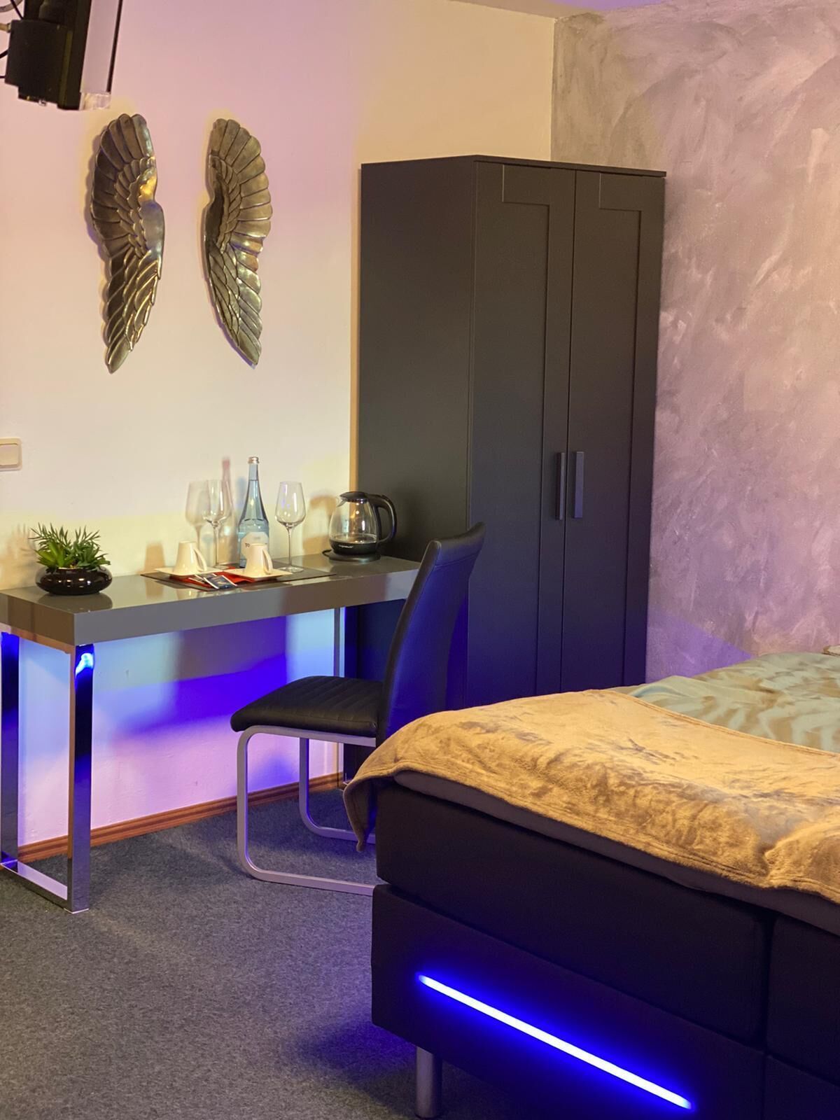 Un dormitorio con cama, escritorio y silla, armario y decoración en la pared.