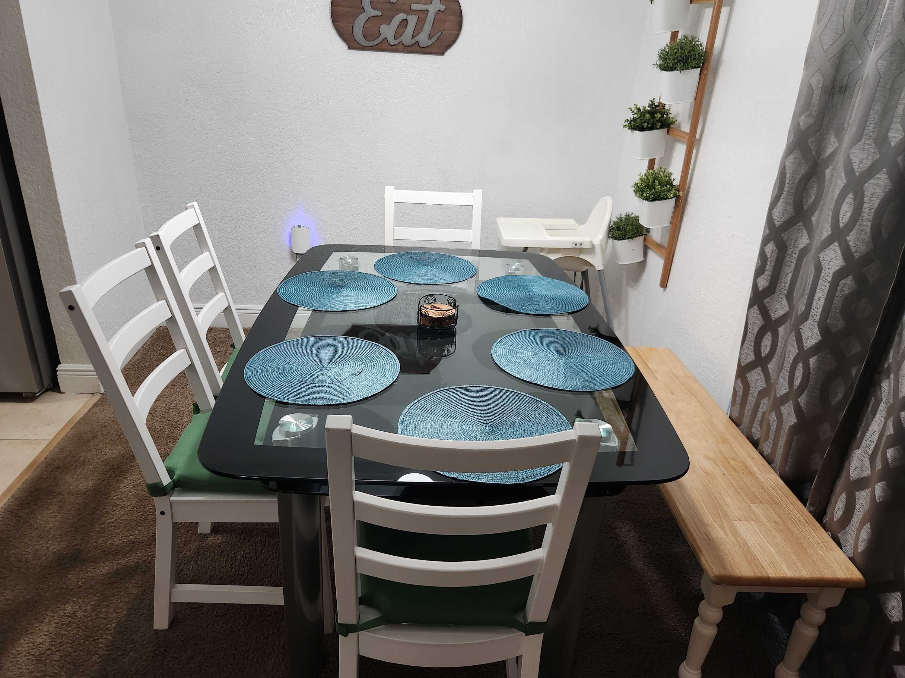 A dining table with blue placemats, white chairs, and a wooden bench.