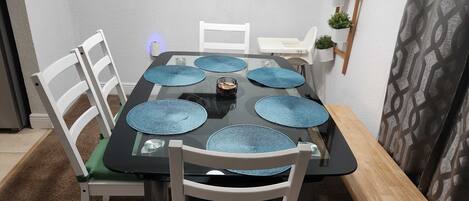 A dining table with blue placemats, white chairs, and a wooden bench.