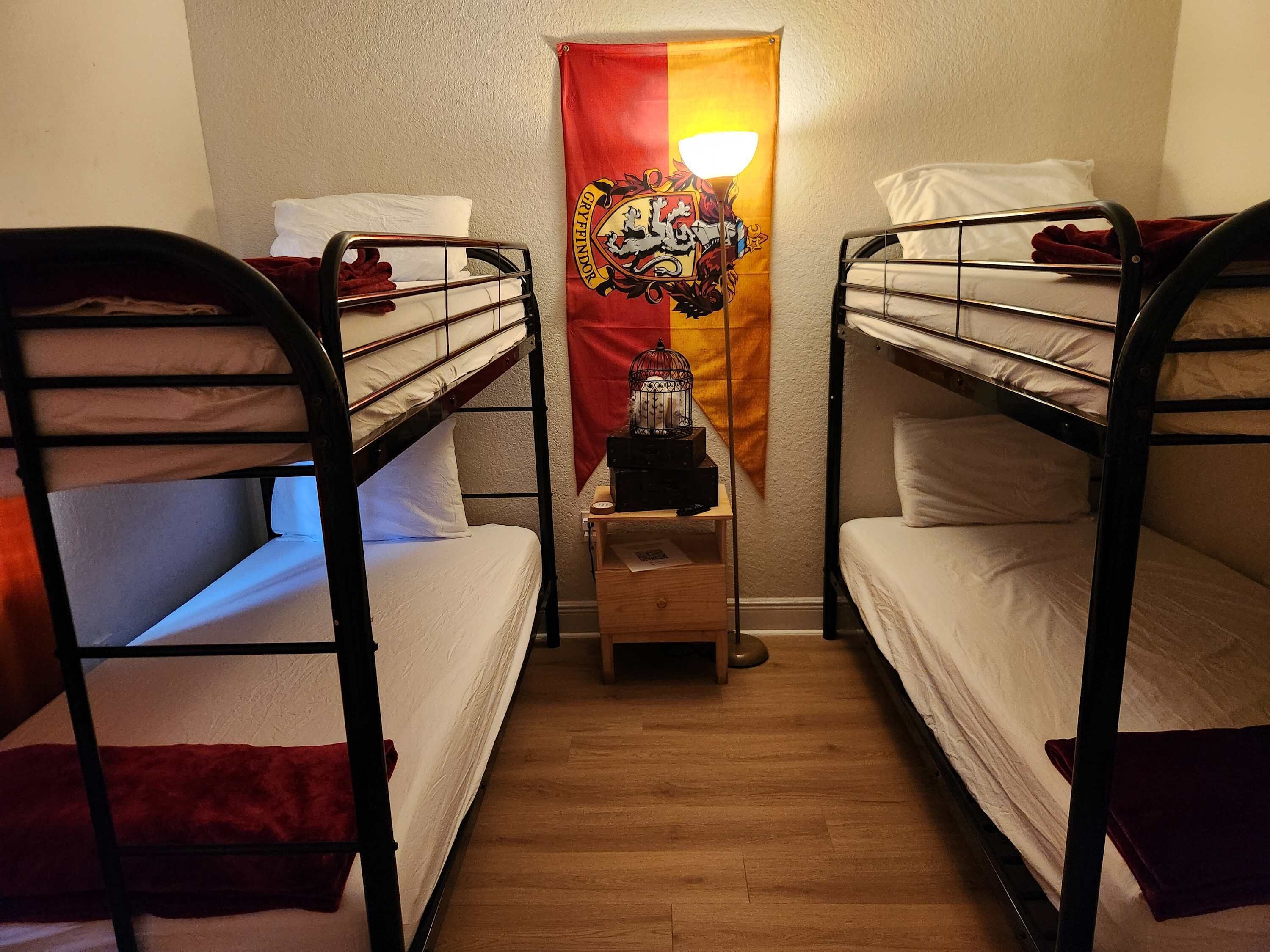 Una habitación con dos literas, una mesita de noche de madera, un cartel decorativo y una lámpara de pie.
