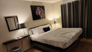A hotel room with a single bed, a desk with a chair, a wall-mounted lamp, a mirror, and a painting of a tiger. - Family-Friendly 2BR Condo Near Universal (Orlando)