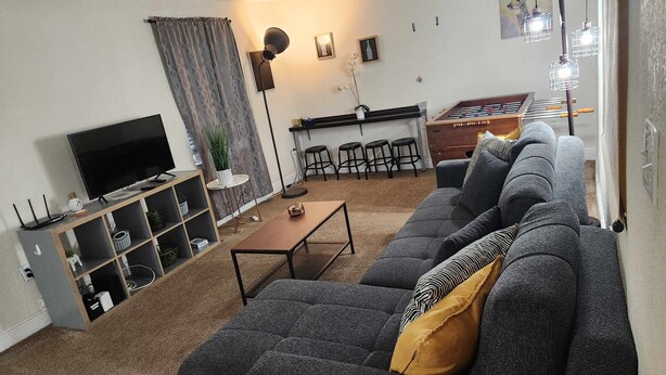 A living room with a sofa, TV, and a small table. There is a kitchen area with stools and a bar counter. - Family-Friendly 2BR Condo Near Universal (Orlando)
