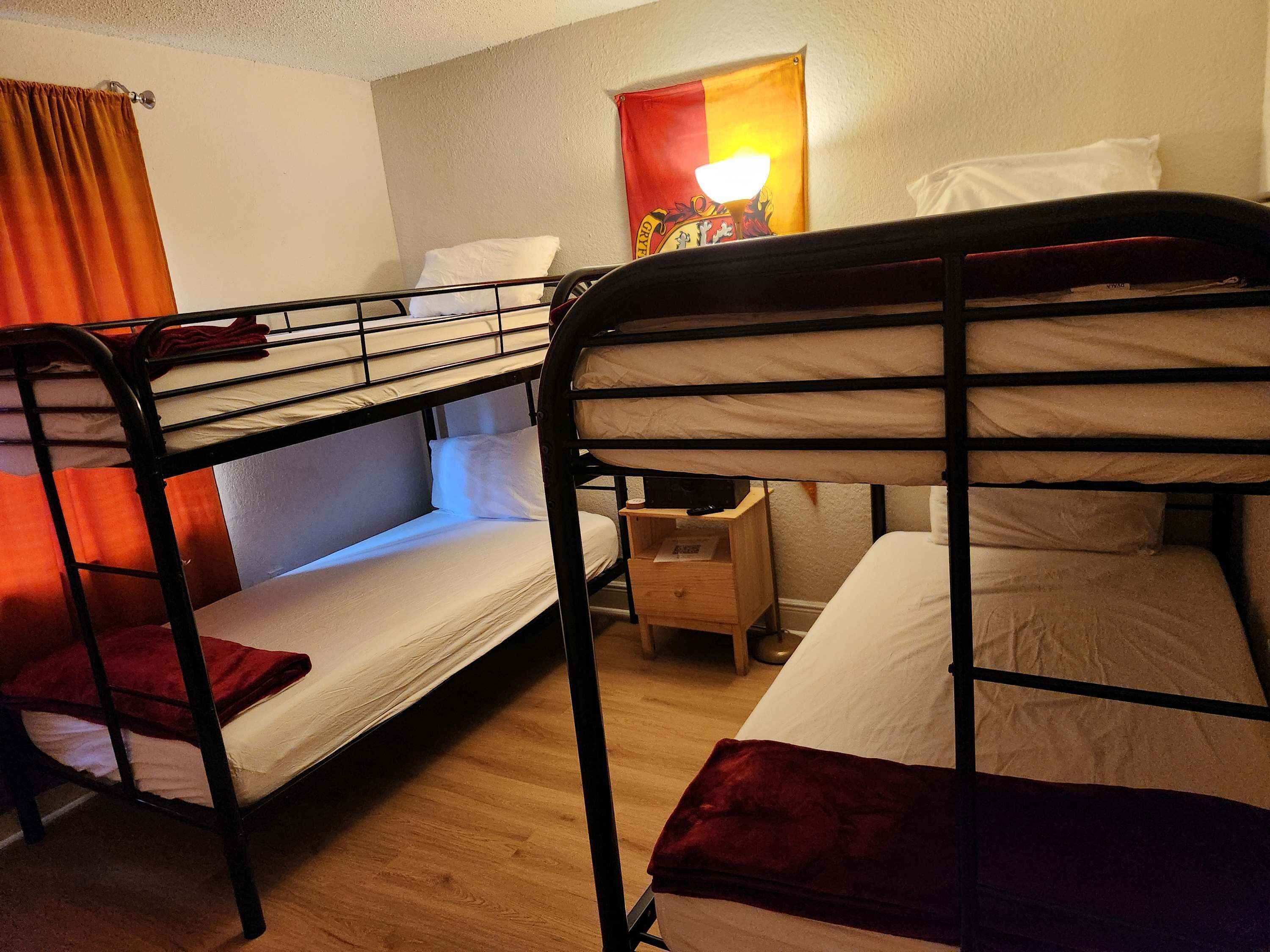 A bunk bed room with a small wooden nightstand, a lamp, and a flag on the wall.