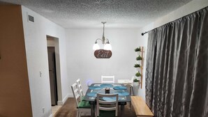 A dining area with a table, chairs, a bench, a ceiling light fixture, and a wall-mounted sign. - Family-Friendly 2BR Condo Near Universal (Orlando)