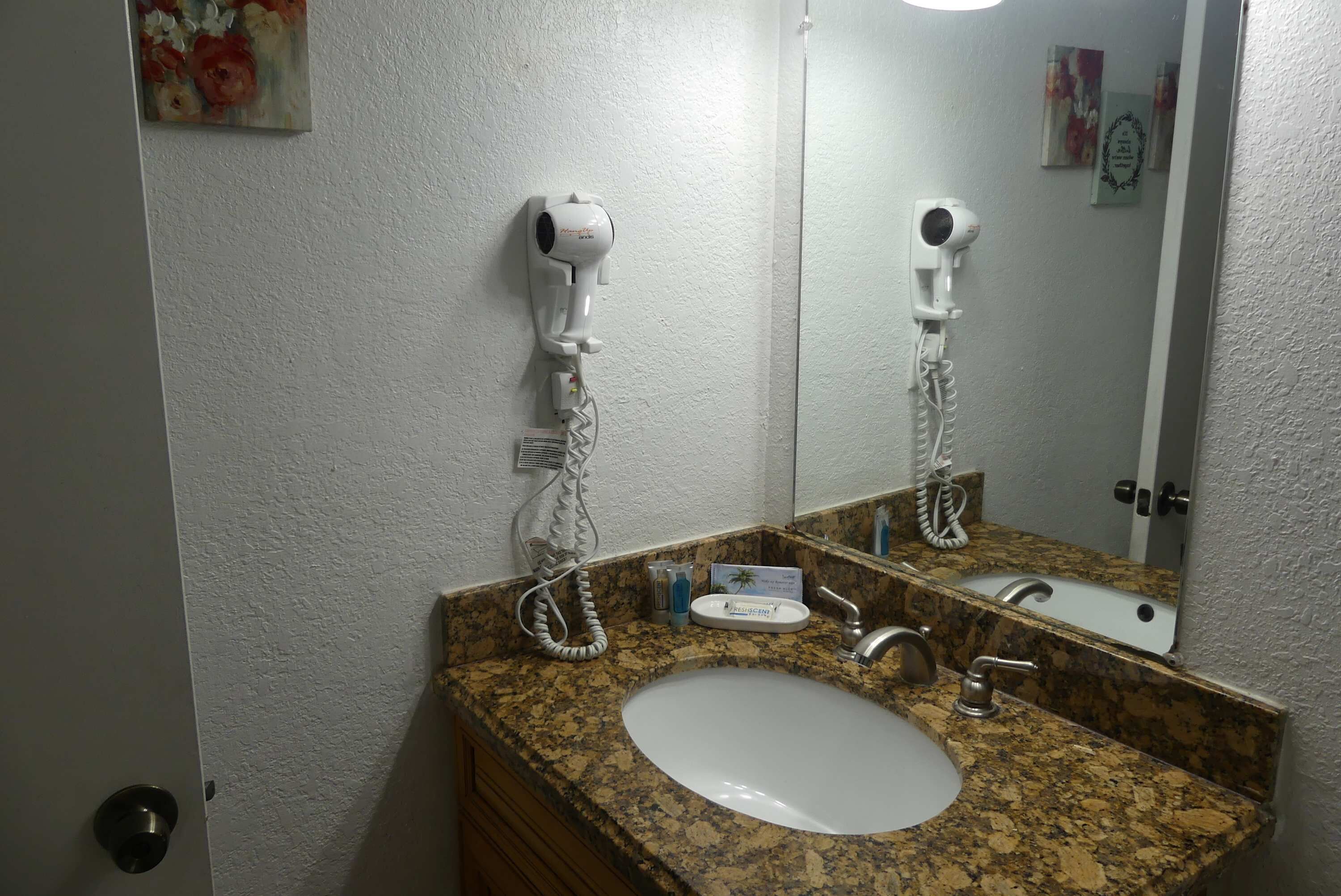 A bathroom with a granite countertop, a white sink, a mirror, and two hair dryers mounted on the wall.