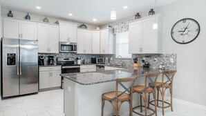 Una cocina moderna con armarios blancos, electrodomésticos de acero inoxidable, una encimera de granito y una isla central con taburetes de bar.