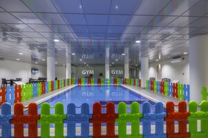 En swimmingpool med färgglada staket, skyltar som visar var gymmet finns och ett kaklat golv.