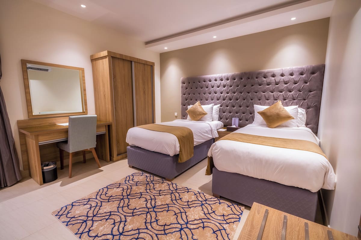 A hotel room with two beds, a desk, a chair, a mirror, and a patterned rug.