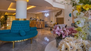 A lobby with a teal sofa, a coffee bar, and floral arrangements. - THE ADDRESS PALACE HOTEL & APARTMENT (Dammam)