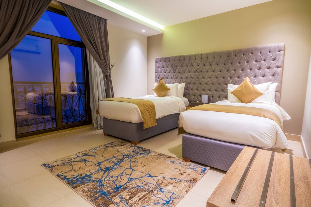 A hotel room with two beds, a large window with curtains, a balcony, and a modern design.