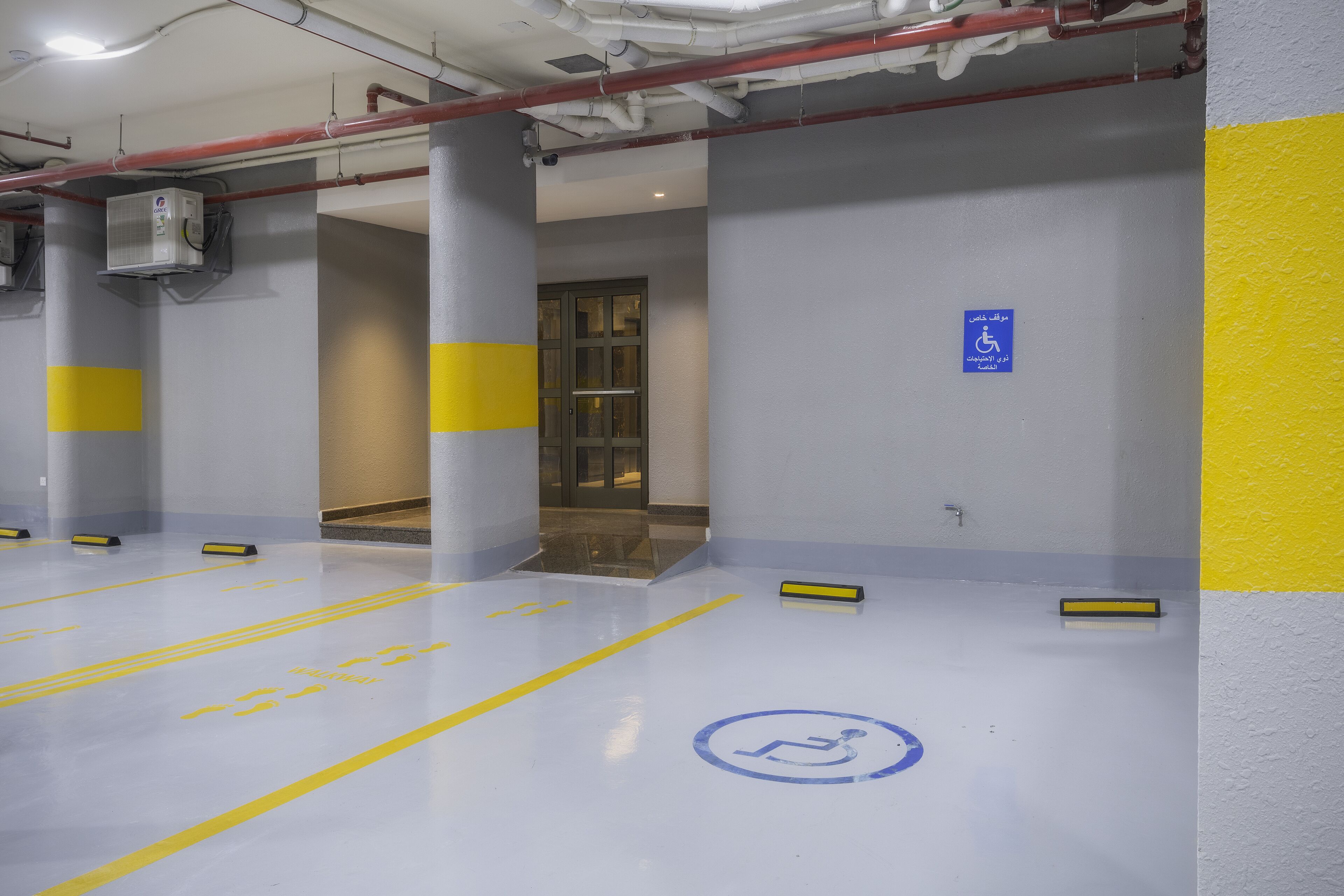 A parking garage with yellow and grey painted areas, a disabled parking sign, and a clean, well-lit environment.