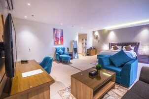 Ett modernt hotellrum med en stor säng, en sittgrupp med en blå soffa och fåtöljer, ett soffbord i trä och en platt-TV.