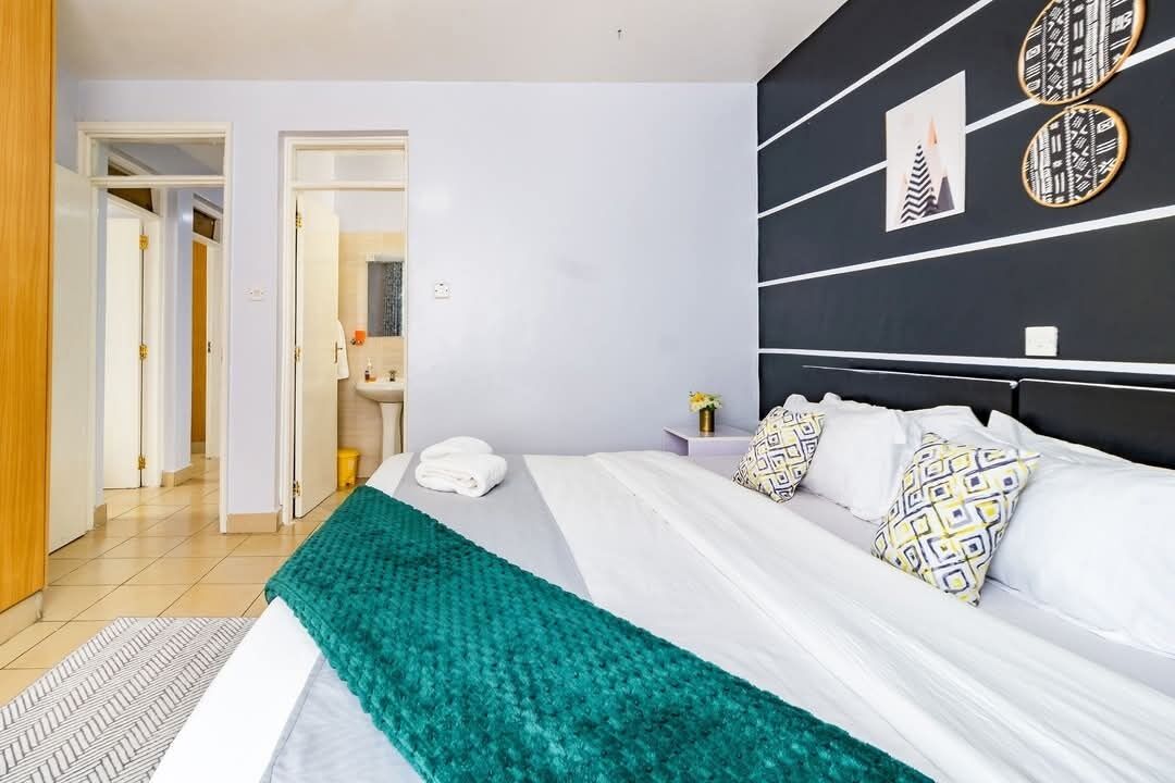 A modern hotel room with a large bed, a black headboard, and a view of the hallway.