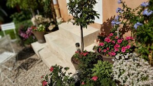 Un jardín con plantas y flores en macetas variadas, entre ellas flores rosadas y blancas, dispuestas en escalones de piedra.