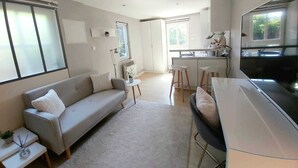 Un espacio habitable moderno y de concepto abierto con sofá, una mesita y una zona de cocina con taburetes.