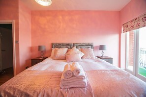 Un dormitorio con cama, almohadas, mesita de noche, lámpara y ventana.
