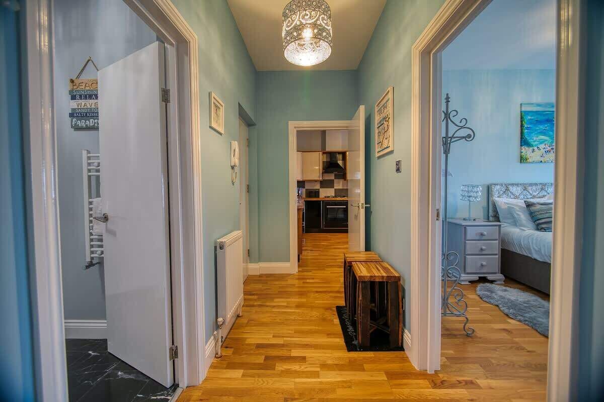 A hallway with wooden flooring, a chandelier, and a bed with a blue bedspread.