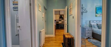 A hallway with wooden flooring, a chandelier, and a bed with a blue bedspread.