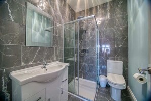 Un baño con ducha de vidrio, lavamanos blanco y retrete.