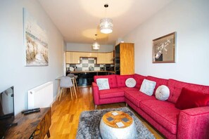 Una sala de estar moderna con un sofá rojo, una mesa de centro y una cocina al fondo.