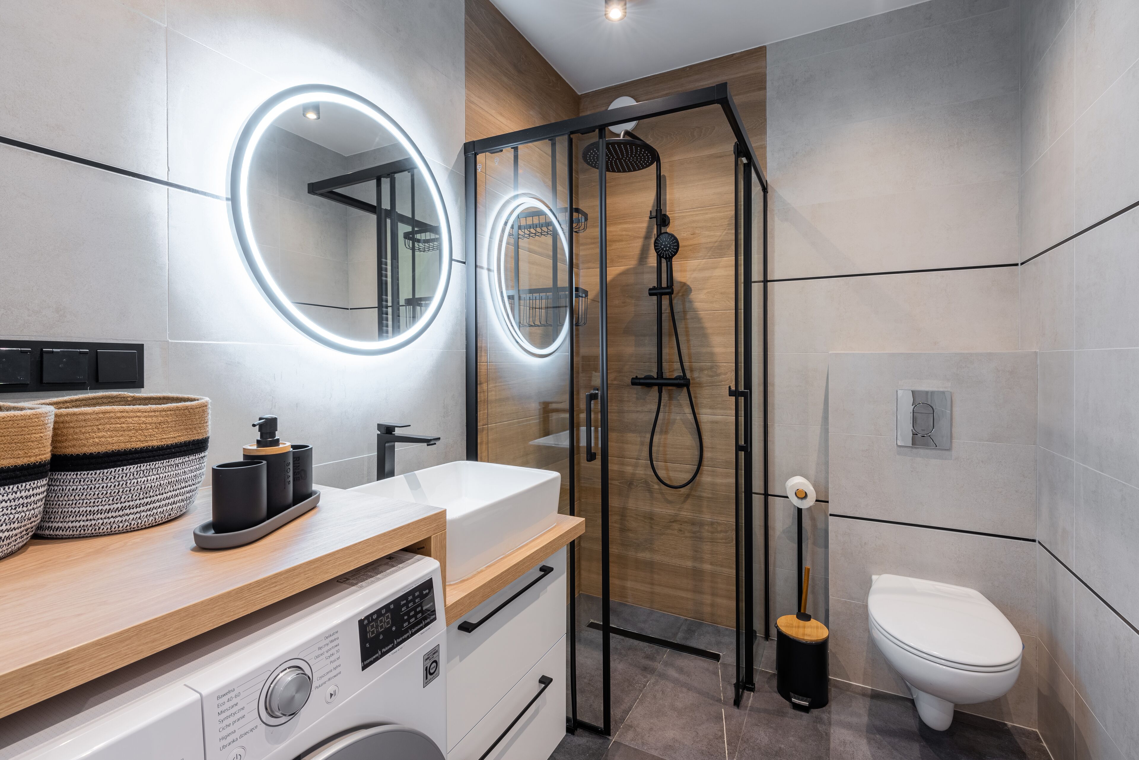 Een moderne badkamer met een ingebouwde wasmachine, een douchecabine van glas en een toilet.