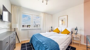 A modern hotel room with a bed, a desk, a chair, a TV, and a window with a view of buildings. - Prywatne apartamenty w Sun & Snow Porta Mare (Kolobrzeg)