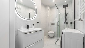 A modern bathroom with a white vanity, a round mirror, a glass shower enclosure, and a toilet. - Prywatne apartamenty w Sun & Snow Porta Mare (Kolobrzeg)