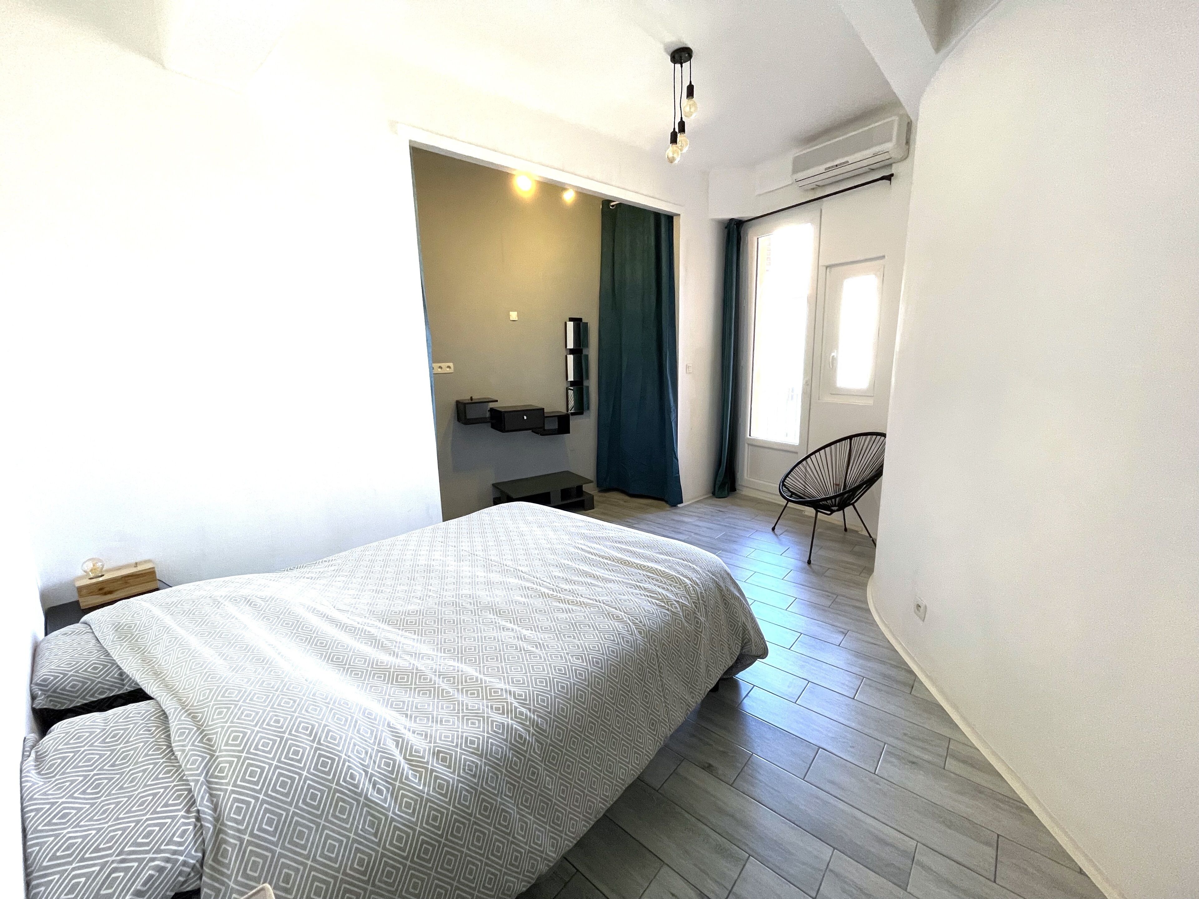 A modern bedroom with a large bed, a chair, a desk, and a window with curtains.