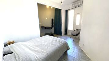 A modern bedroom with a large bed, a chair, a desk, and a window with curtains.